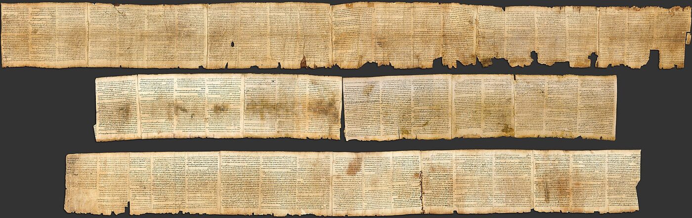 A photograph of a long parchment scroll laid out in four horizontal strips against a dark ground, each strip ruled into columns of ancient Hebrew script, the parchment brown and torn along its edges.