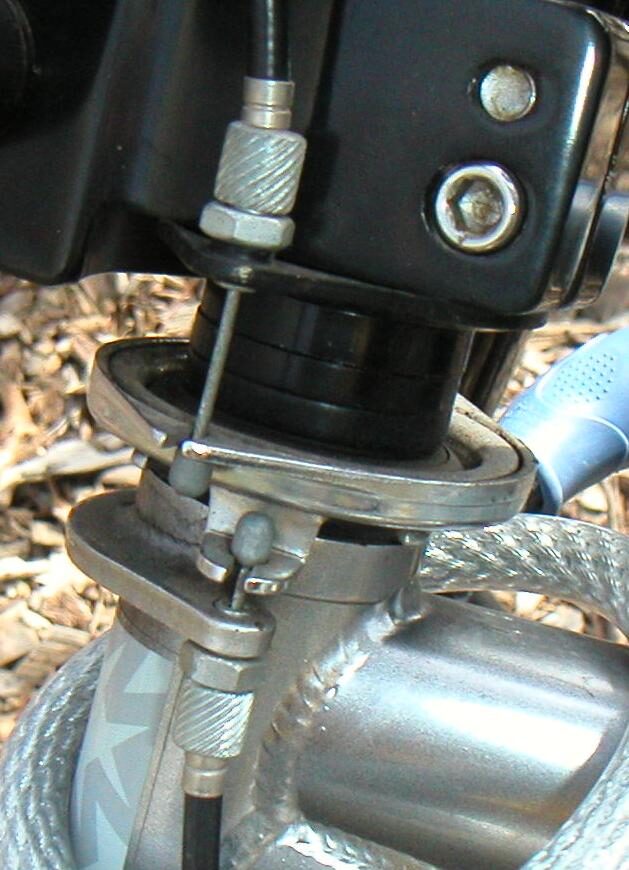 Close-up of a bicycle stem and head tube showing a two-plate rotor mechanism seated on a bearing around the steerer, with a brake cable entering from above and another leaving below.