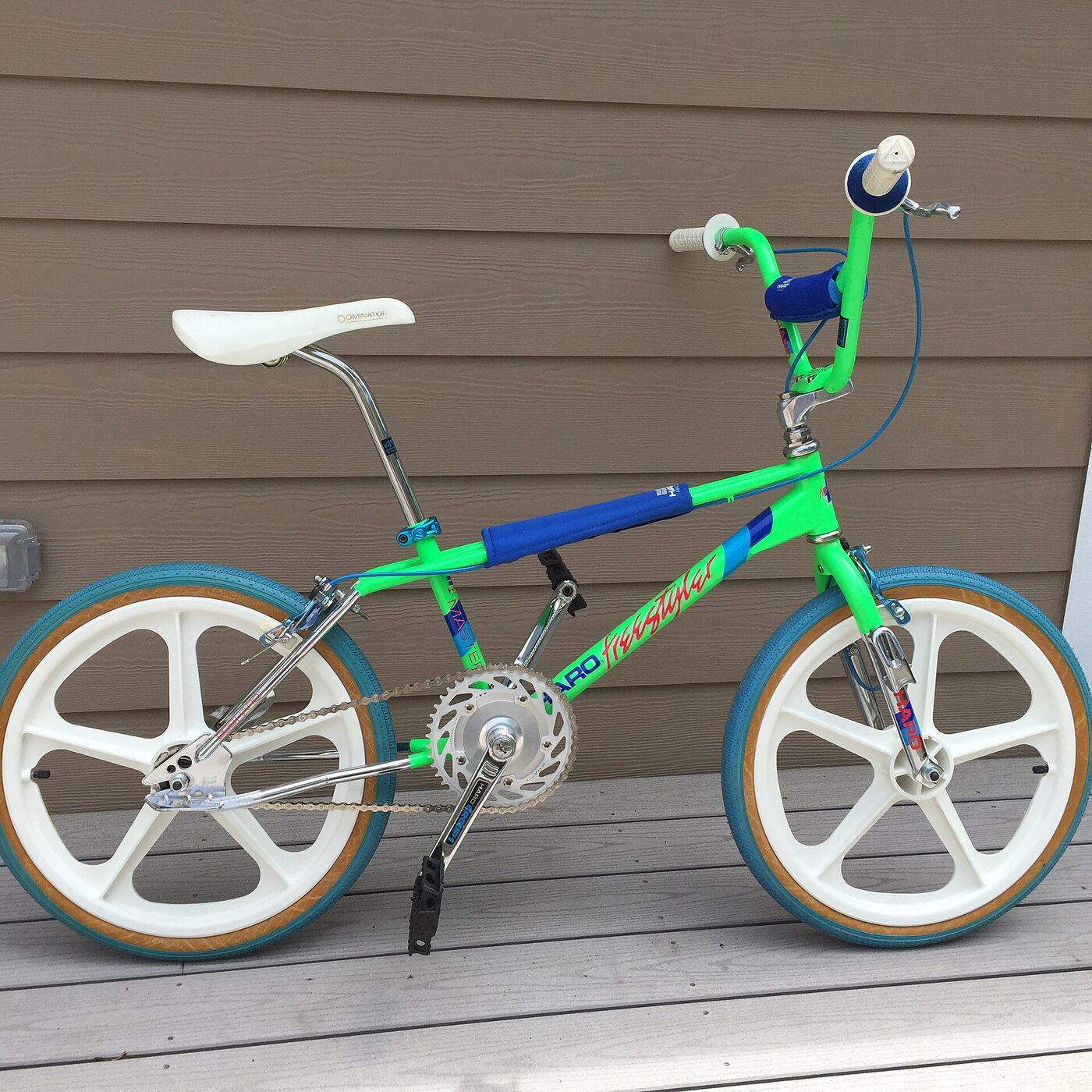 A 1980s freestyle BMX bicycle in bright neon green with twenty-inch wheels, white five-spoke mag wheels, a blue padded crossbar and stem pad, a white saddle, and cable-operated brakes front and rear.
