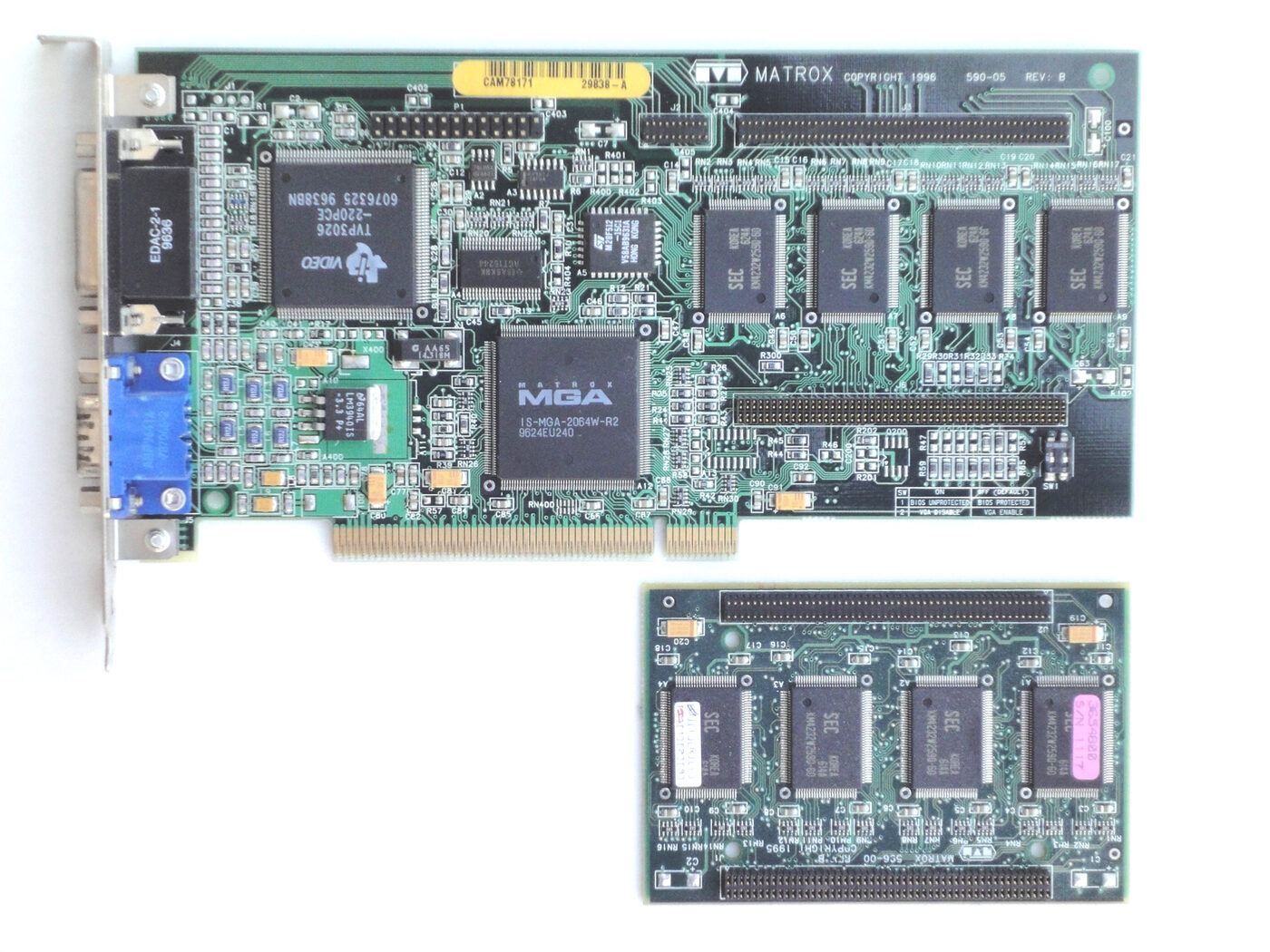 A green PCI expansion card lying on a white background, with a large square Matrox MGA graphics chip in the centre, four memory chips in a row, a metal bracket carrying blue and dark monitor connectors, and a smaller separate memory daughterboard placed below it.