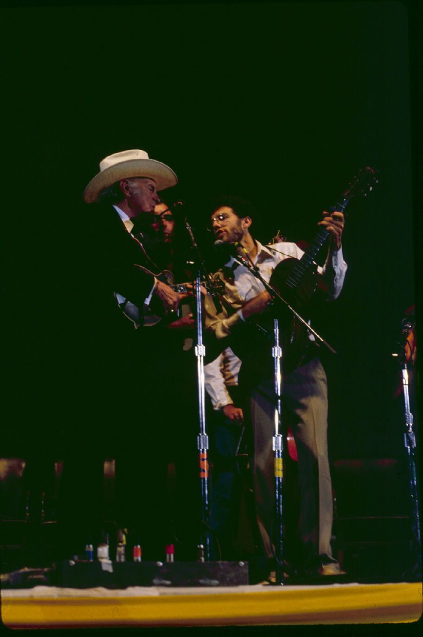 Photograph of a band of men in suits and hats performing on a stage with mandolin, fiddle, guitar and banjo.
