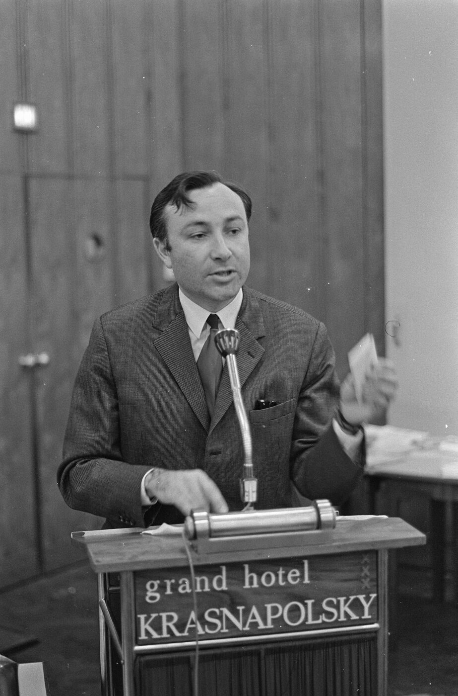 Black-and-white photograph of a 1967 Alcoholics Anonymous meeting in an Amsterdam hall, a man speaking at a table before a seated audience.