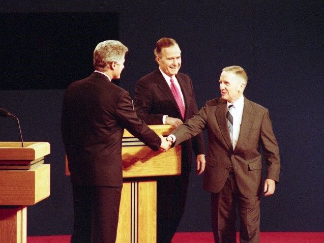 Three men in suits shaking hands across a lectern on a televised debate stage in 1992.