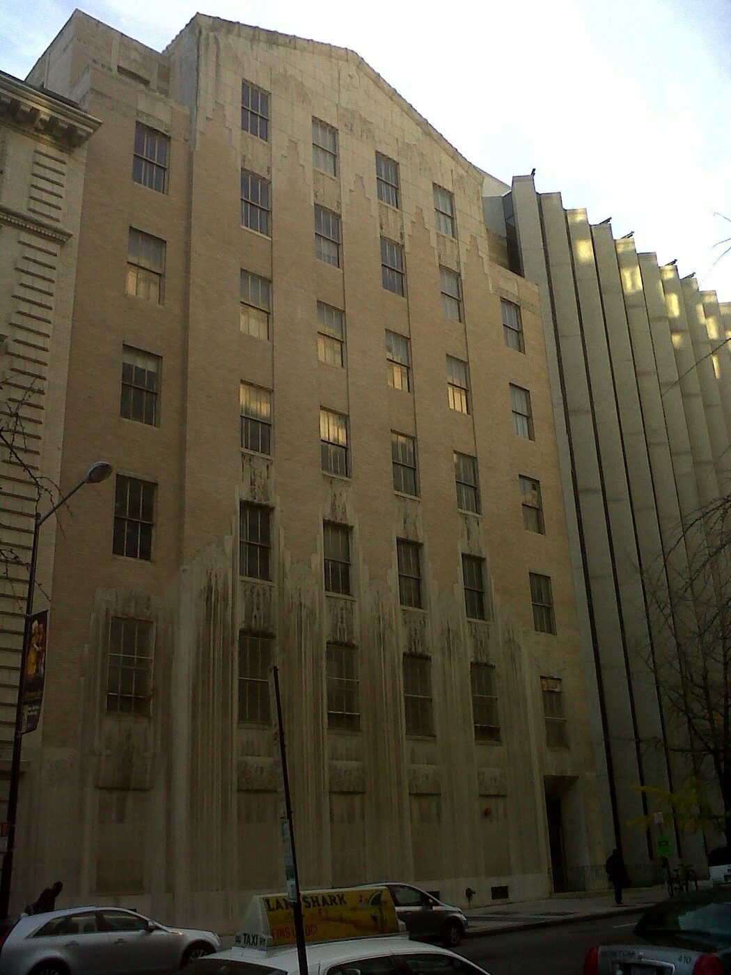 A tall masonry office building with vertical piers and recessed windows, seen from street level against a pale sky.