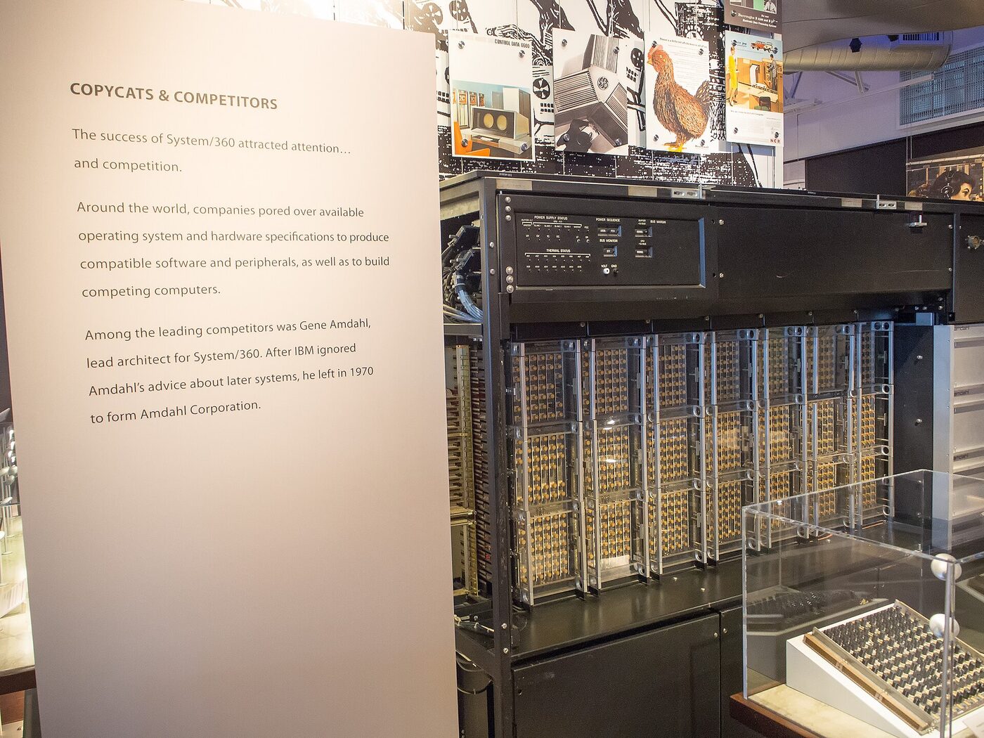 Museum exhibit: an opened mainframe cabinet with racks of gold-pinned circuit modules behind clear panels and a status panel above, beside a display board headed "Copycats & Competitors" describing Gene Amdahl leaving IBM in 1970.