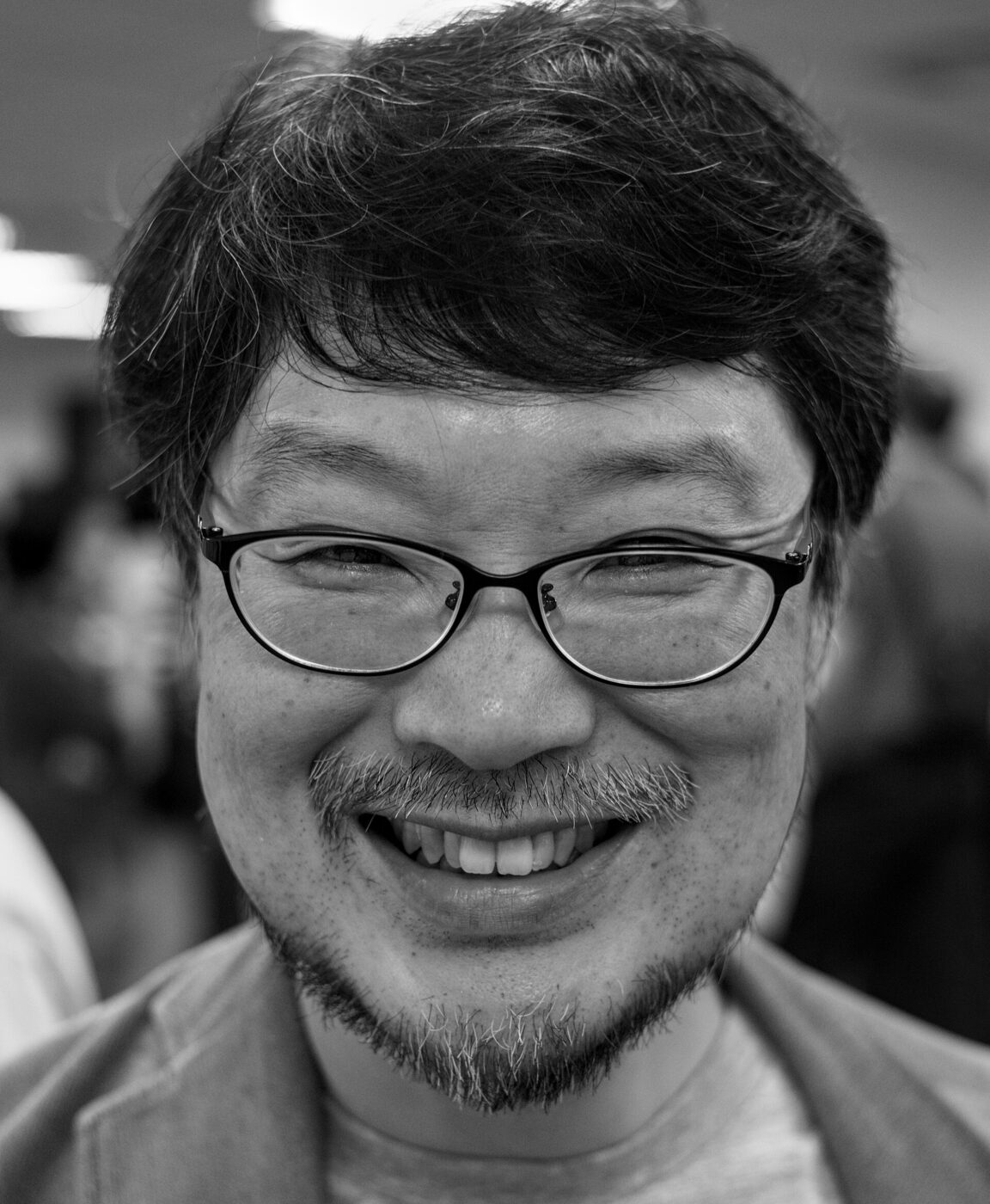 Black-and-white close-up portrait of a smiling bespectacled man with dark hair, a moustache and a short beard.