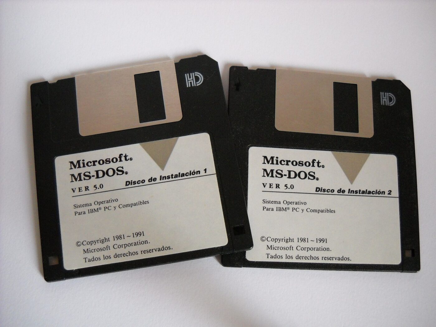Two 3.5-inch high-density floppy disks lying on a pale surface, labelled Microsoft MS-DOS VER 5.0, Disco de Instalacion 1 and 2, Sistema Operativo Para IBM PC y Compatibles, copyright 1981-1991.