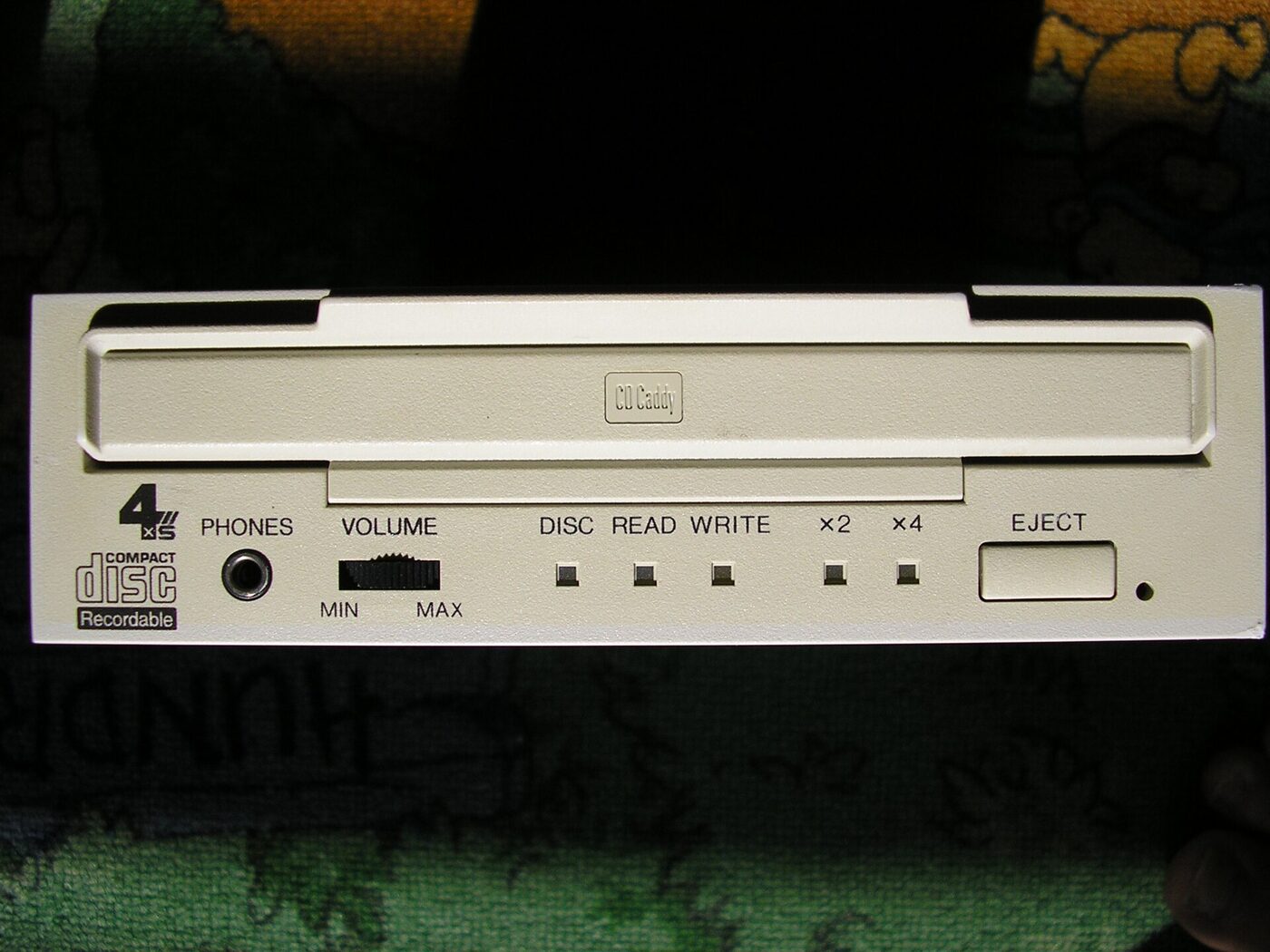 The cream-coloured front panel of a half-height computer drive, with a wide horizontal slot for a CD caddy, a headphone socket, a volume control, indicator lights and an eject button.