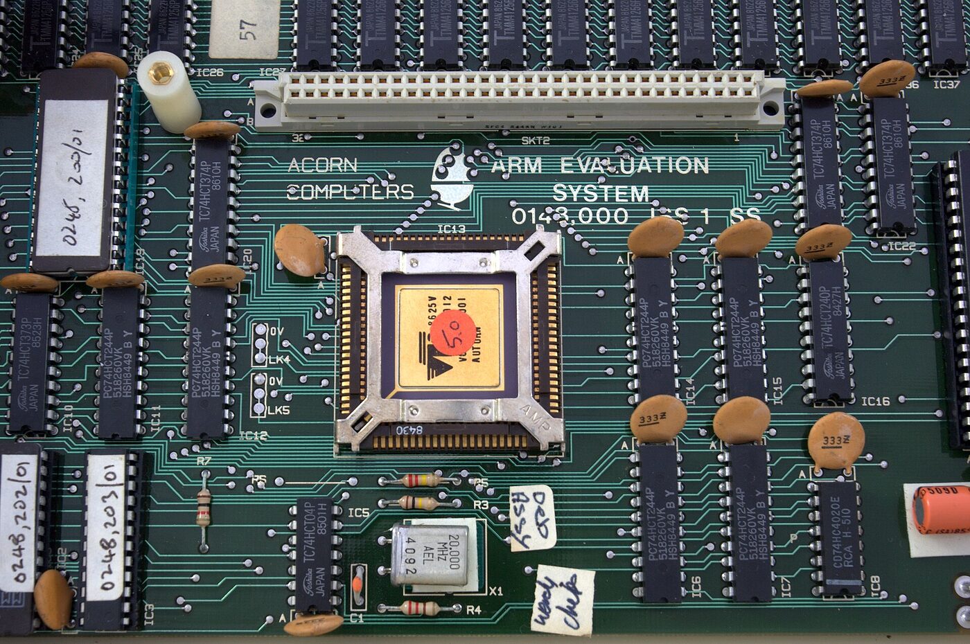 Close-up of a green circuit board silkscreened “Acorn Computers ARM Evaluation System”, with a gold-topped ceramic chip in a metal socket at its centre surrounded by rows of memory and logic chips.