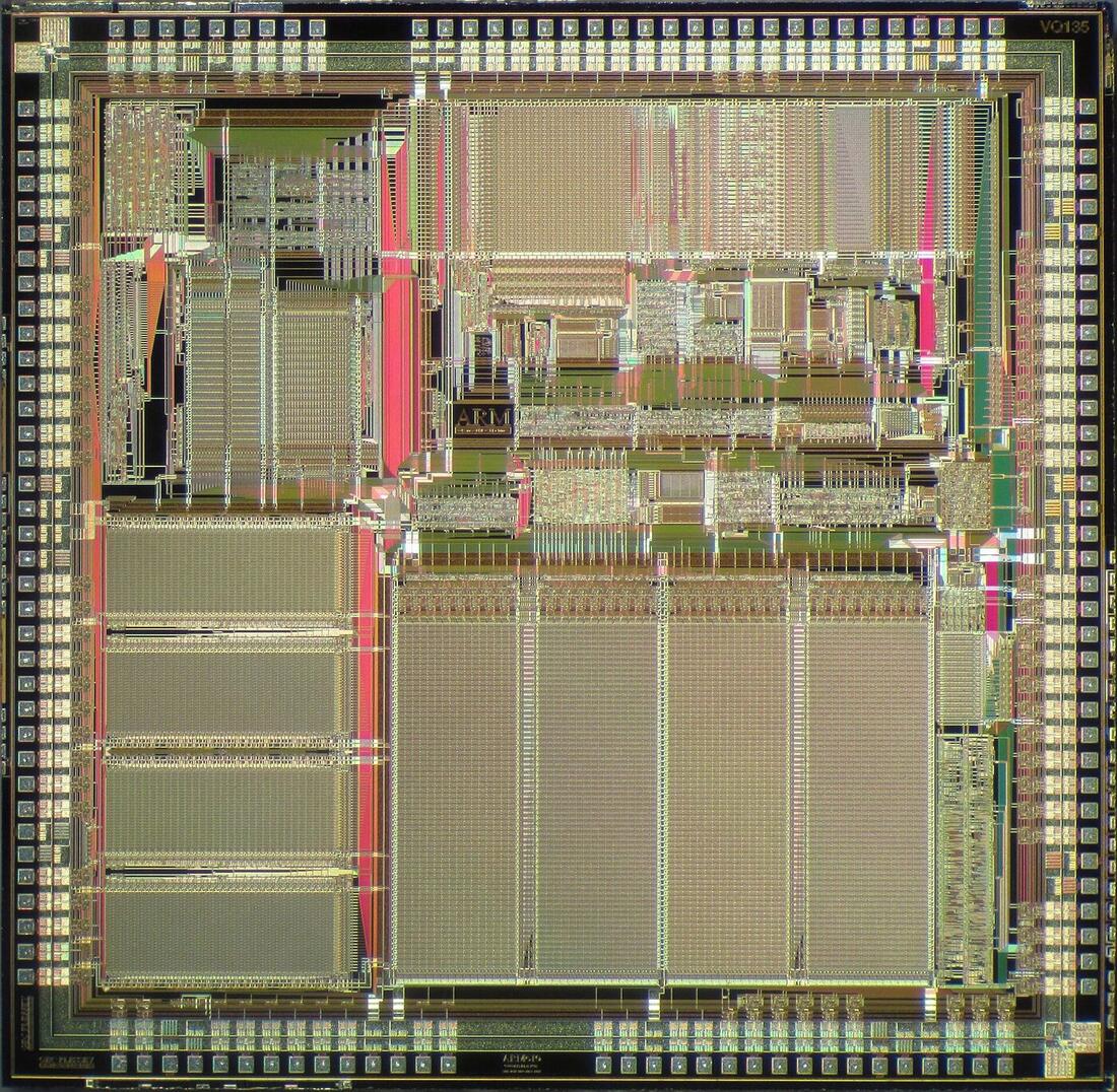 Microscope photograph of a square silicon die showing large regular memory blocks, denser irregular logic, and a border of bond pads.