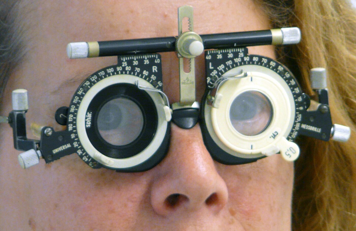 An adjustable metal trial frame for eye examinations, with rotatable lens cells, axis scales and screw adjustments for pupillary distance.