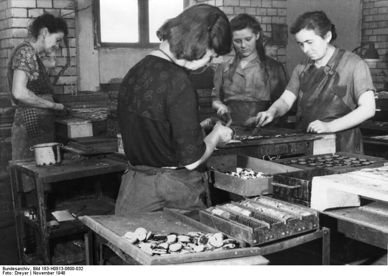 Black-and-white factory photograph from 1948 of workers at long benches preparing spectacle lens blanks for grinding and polishing.
