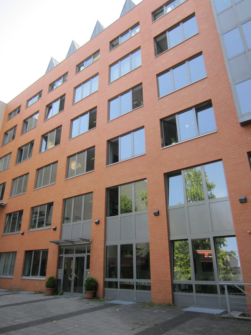 The front of a modern red-brick archive building of five storeys with large grey-framed windows and a glazed ground floor, seen from the paved forecourt.
