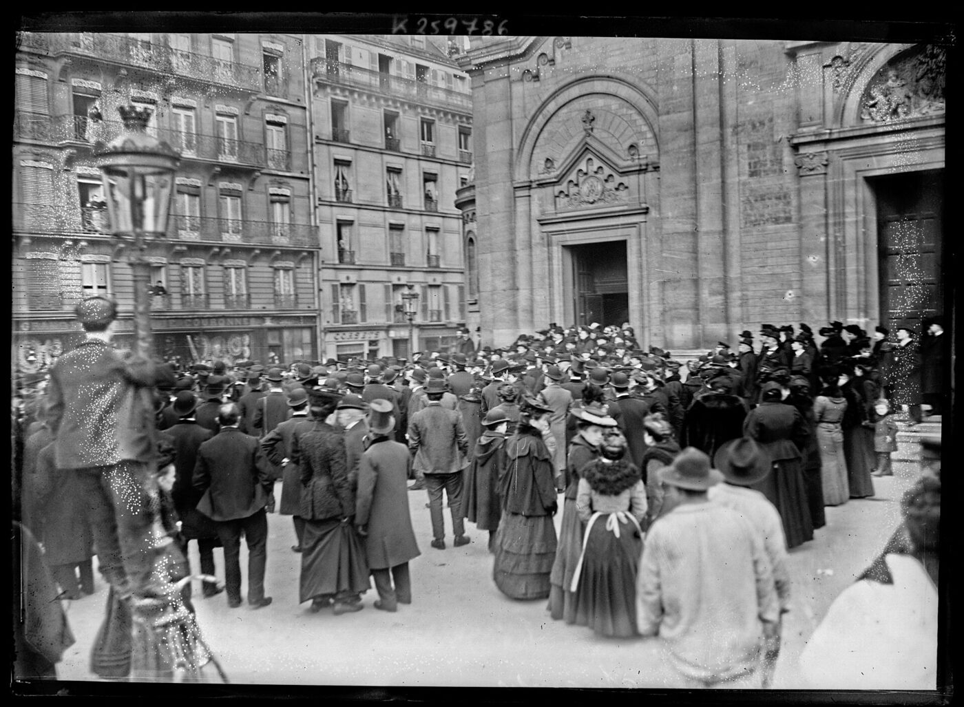 Black-and-white 1906 press photograph of a dense crowd in hats and long coats filling the street in front of a Paris church doorway.