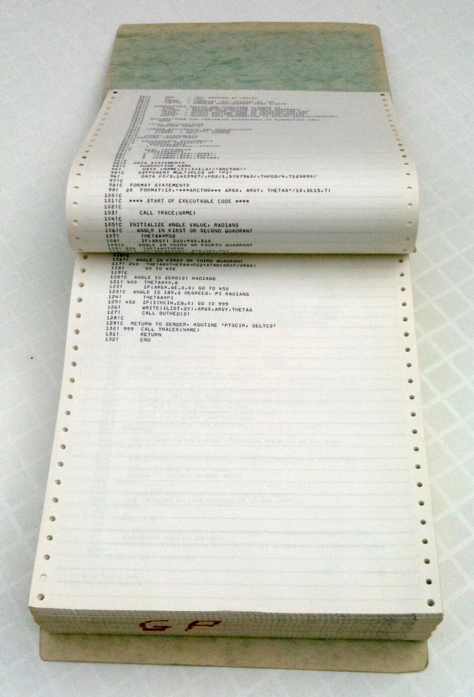 A thick stack of continuous fan-fold computer paper in a stiff printout binder, opened flat to show a page of line-printer output with numbered source lines.