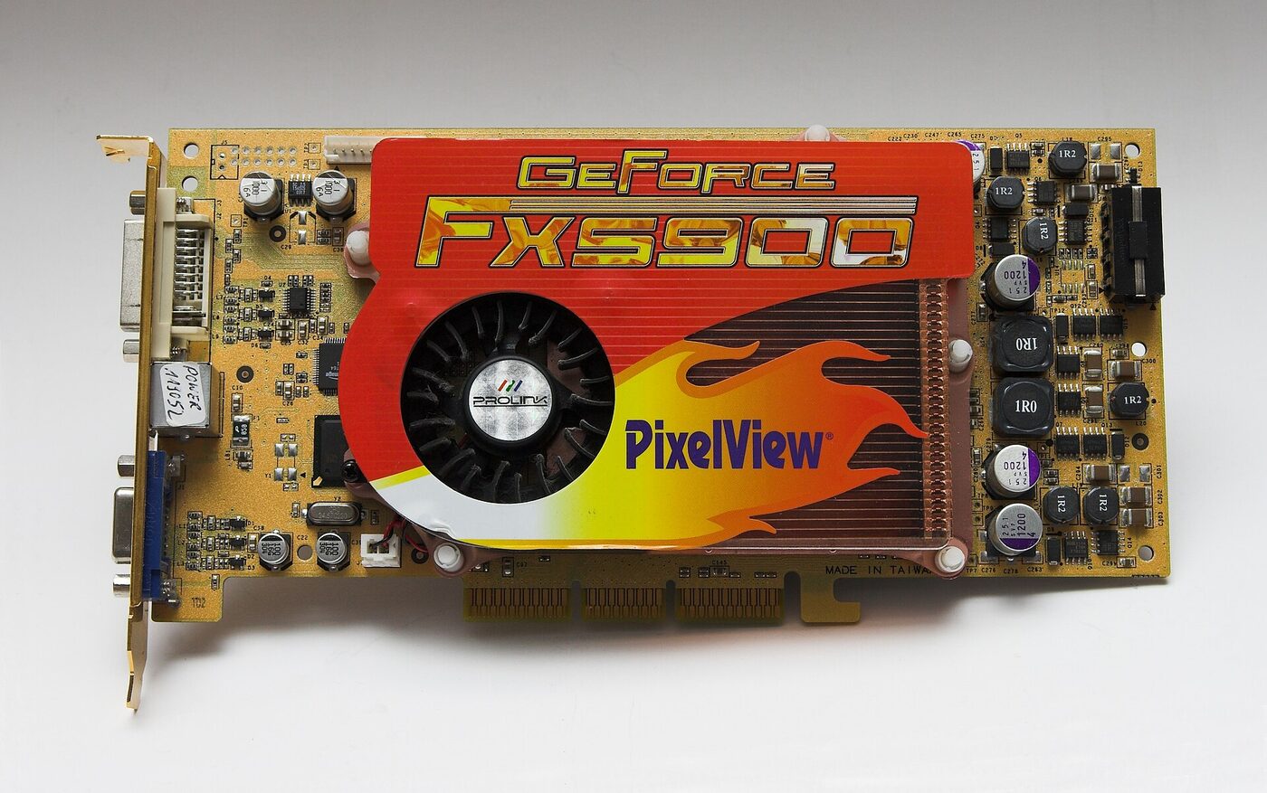 A gold-coloured printed circuit board graphics card lying on a pale surface, with a red, orange and yellow 'GeForce FX5900 PixelView' shroud and cooling fan over the processor, a copper heatsink beside it, DVI and VGA connectors on the metal bracket at the left, and an AGP edge connector along the bottom.