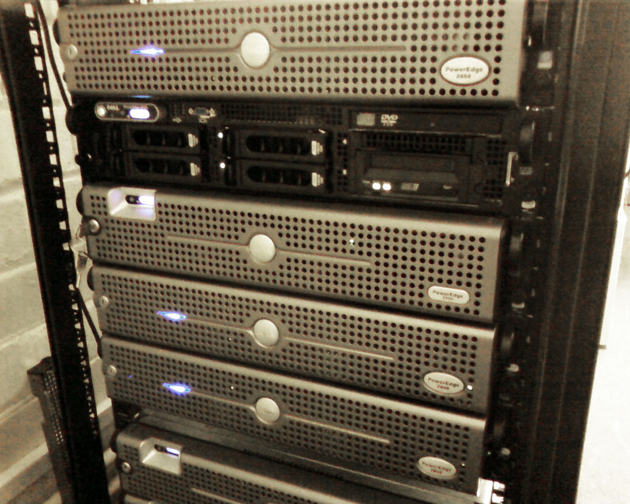 Several rack-mounted Dell PowerEdge servers stacked in an open cabinet against a painted brick wall.