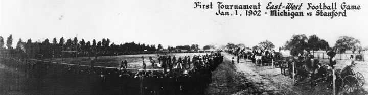 A wide black-and-white photograph of an American football game in 1902, players massed on an open field with spectators standing along the sidelines.