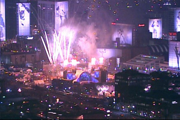 Distant night view of downtown Salt Lake City with fireworks bursting above a brightly lit outdoor stage