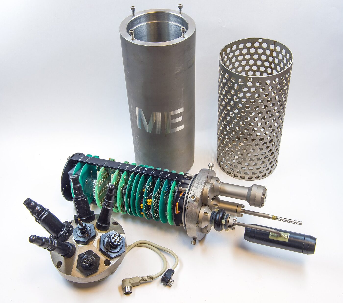 The separated components of an oceanographic probe laid out on a plain white background: a machined metal pressure cylinder, a perforated protective cage, a bulkhead of sealed cable connectors and a stack of circular green circuit boards carrying sensor probes.