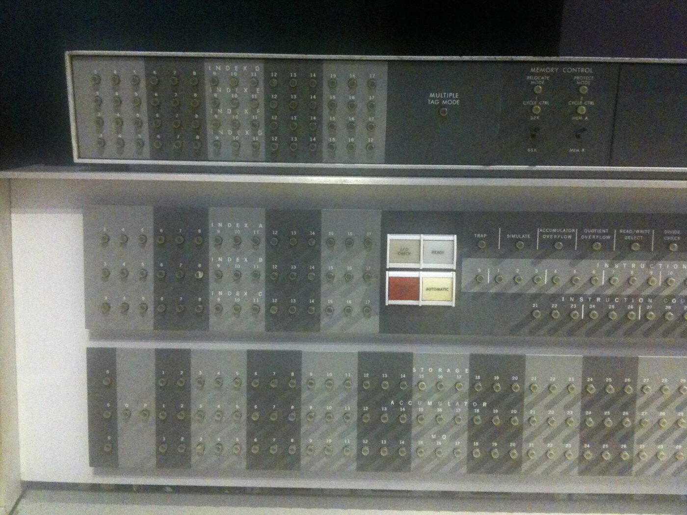 A large 1960s mainframe control console covered in rows of small indicator lamps, toggle switches and labelled register displays.
