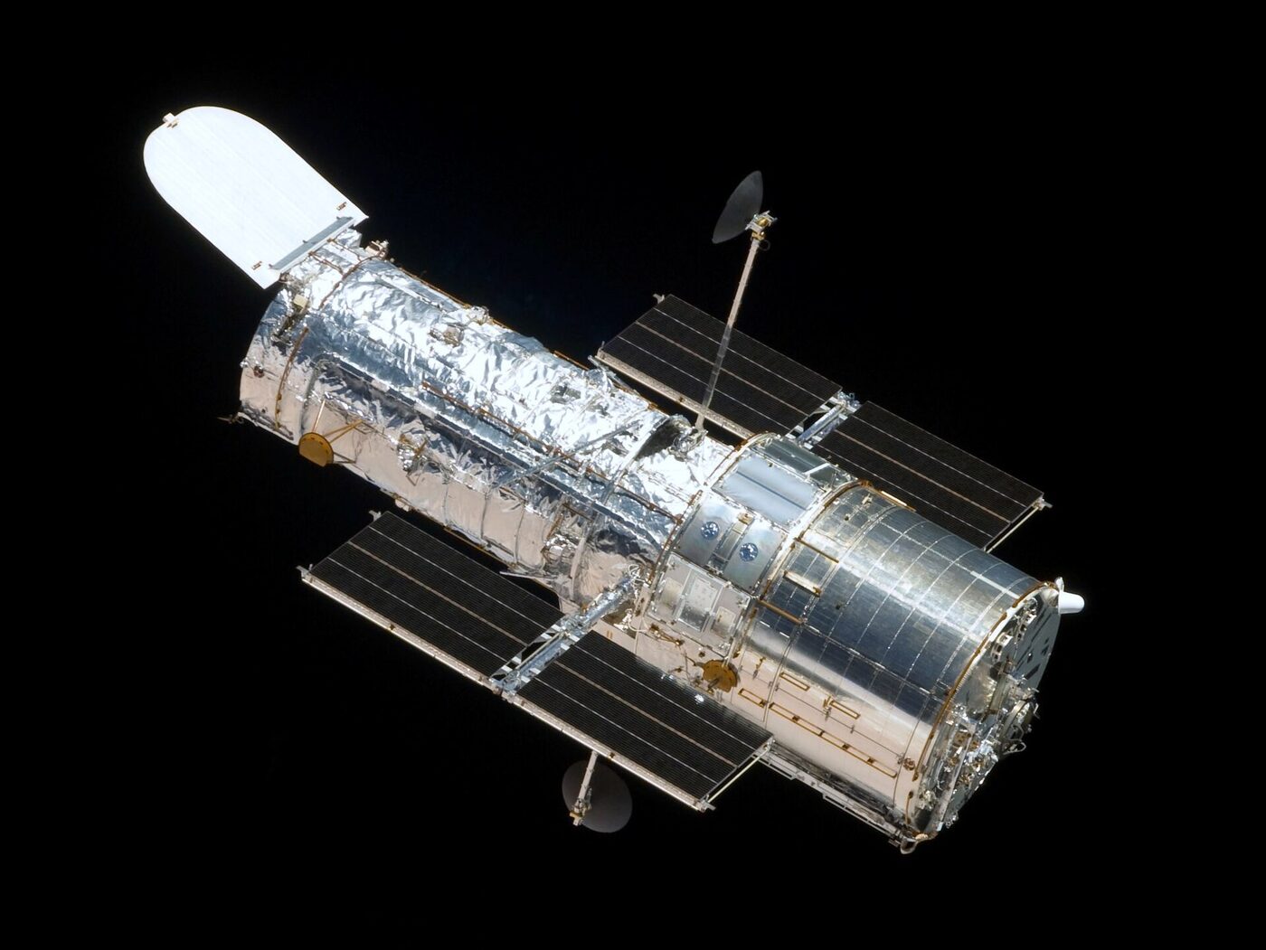 A cylindrical space telescope with a wide aperture door at one end and two long rectangular solar panels, photographed in orbit against the black of space.