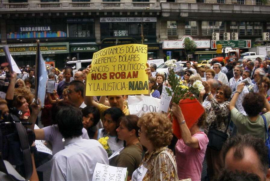 Photograph of a crowd of demonstrators with hand-lettered placards outside a bank building in Buenos Aires.
