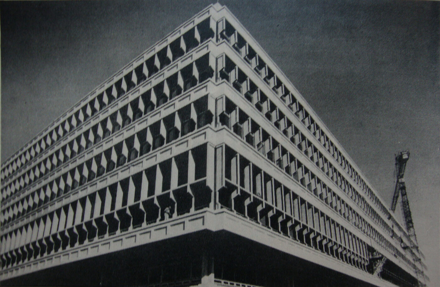 Black-and-white photograph of a large modernist university building under construction, its concrete frame and window bays exposed.