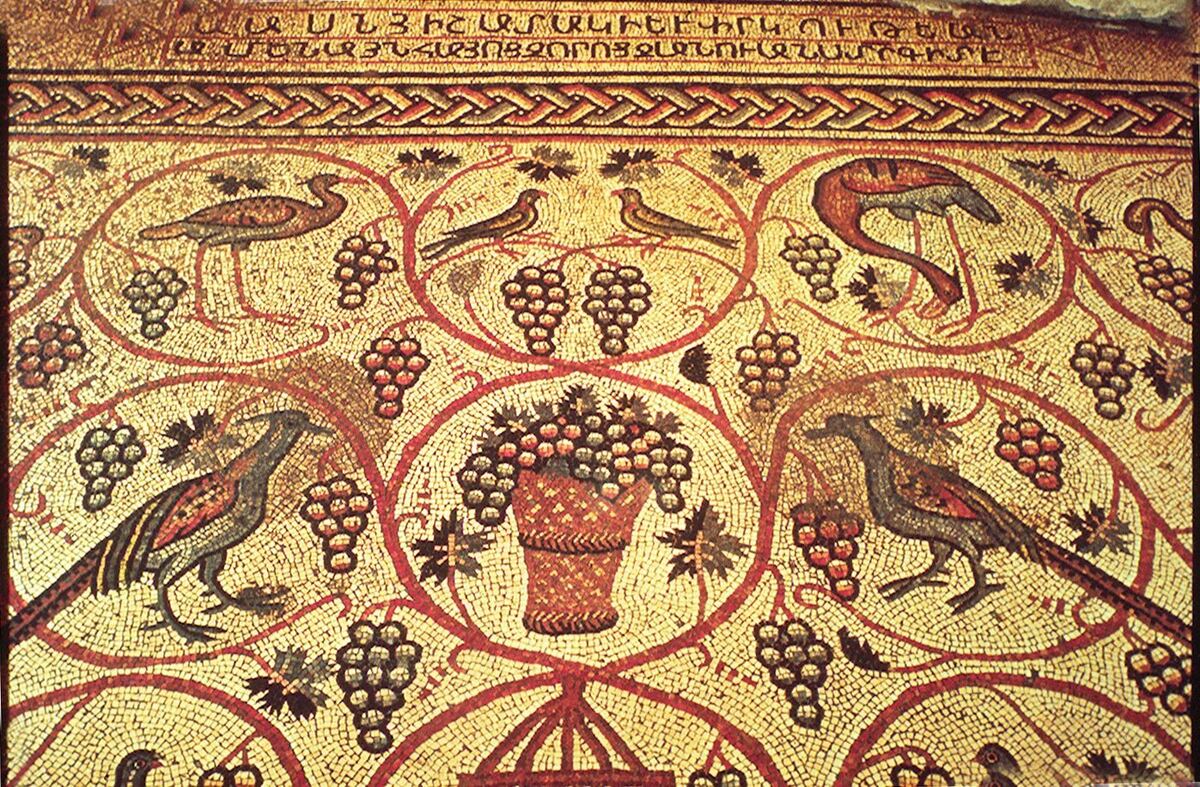 A mosaic pavement of birds and grape clusters within red vine scrolls, with two lines of Armenian capital letters in a border along the top edge.