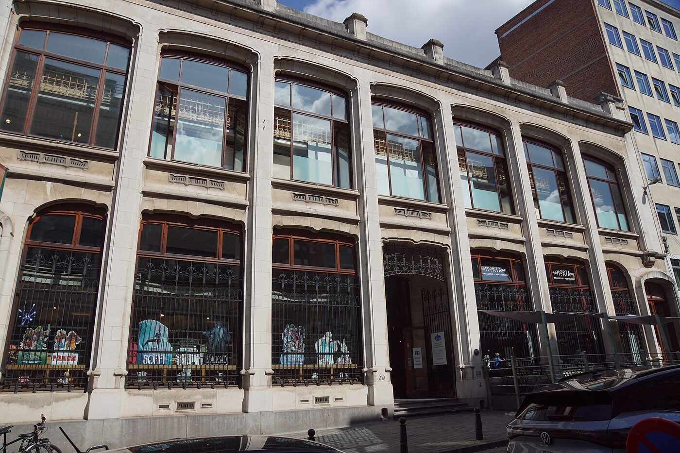 Stone and glass Art Nouveau façade of three storeys with tall arched windows, comic-strip display panels visible behind the ground-floor railings and a street number 20 beside the entrance.