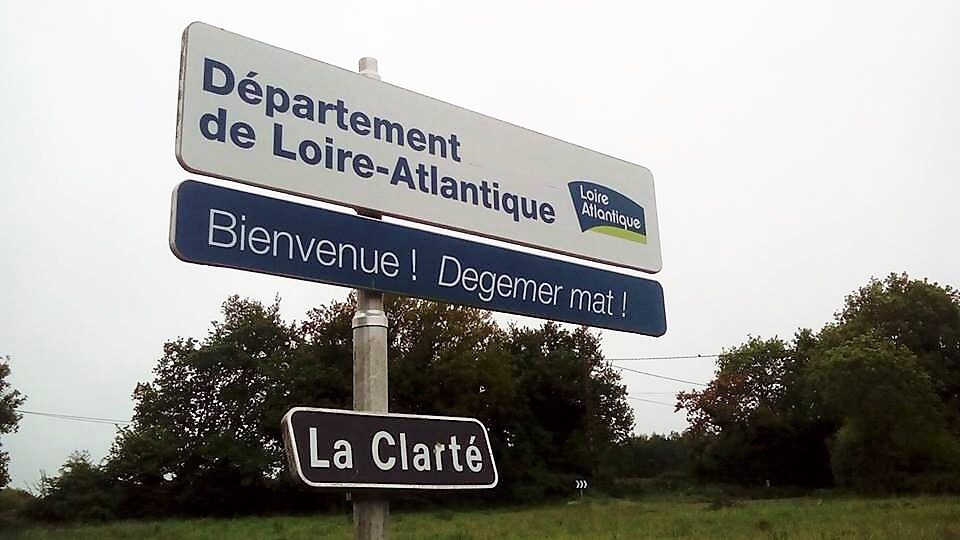 A roadside sign reading Département de Loire-Atlantique above a blue panel reading Bienvenue ! Degemer mat !, with a smaller plate below naming the hamlet La Clarté.