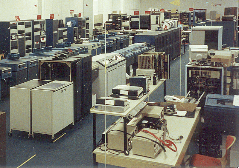 A 1991 computer room with rows of tall minicomputer cabinets and benches of test equipment in the foreground.