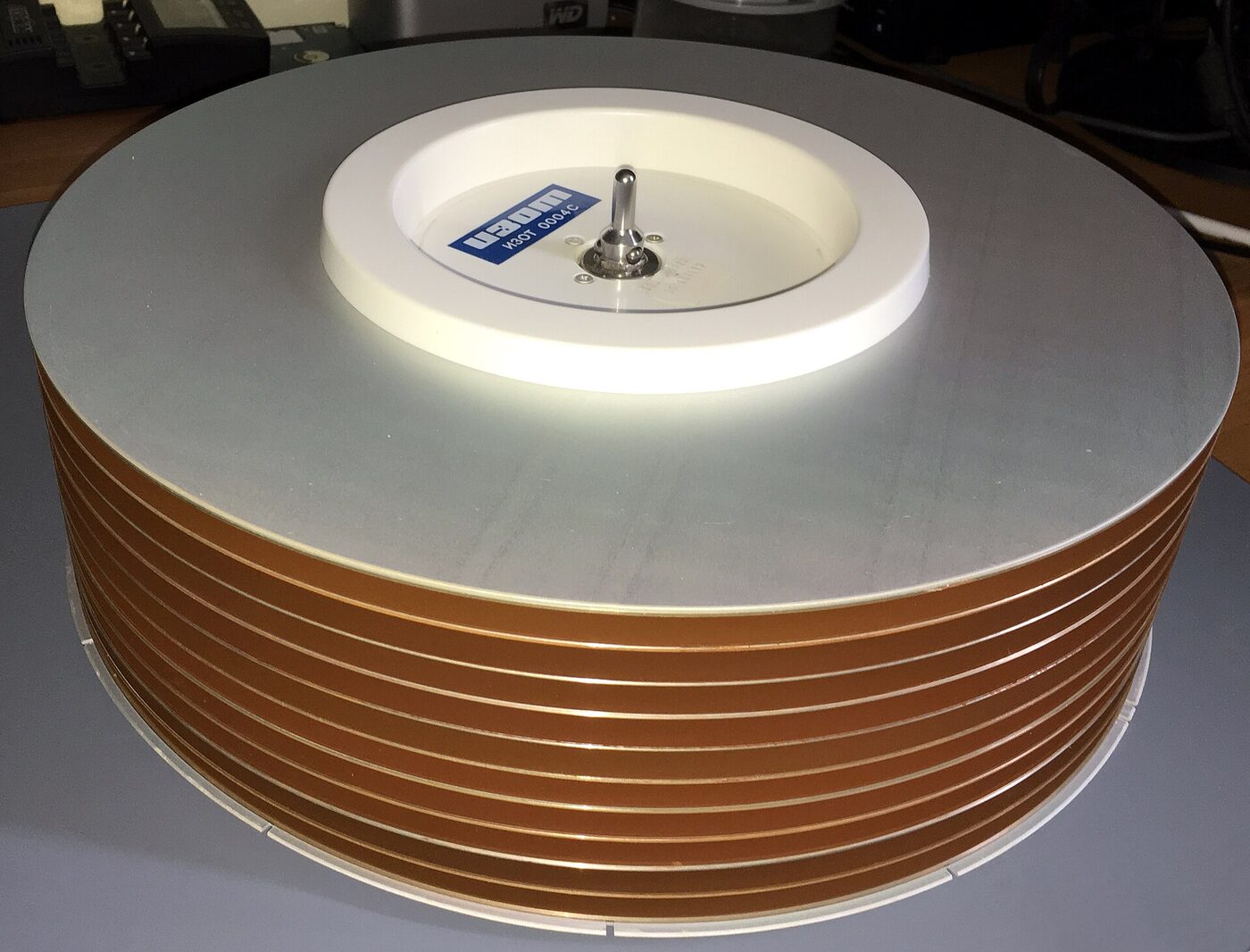 A stack of large circular magnetic disk platters on a white central hub, the hub carrying a blue IZOT label reading ИЗОТ 0004С, standing on a desk.