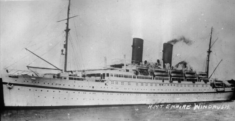 Black and white broadside photograph of a two-funnelled passenger liner under way at sea, with the name H.M.T. Empire Windrush lettered across the lower right of the print.