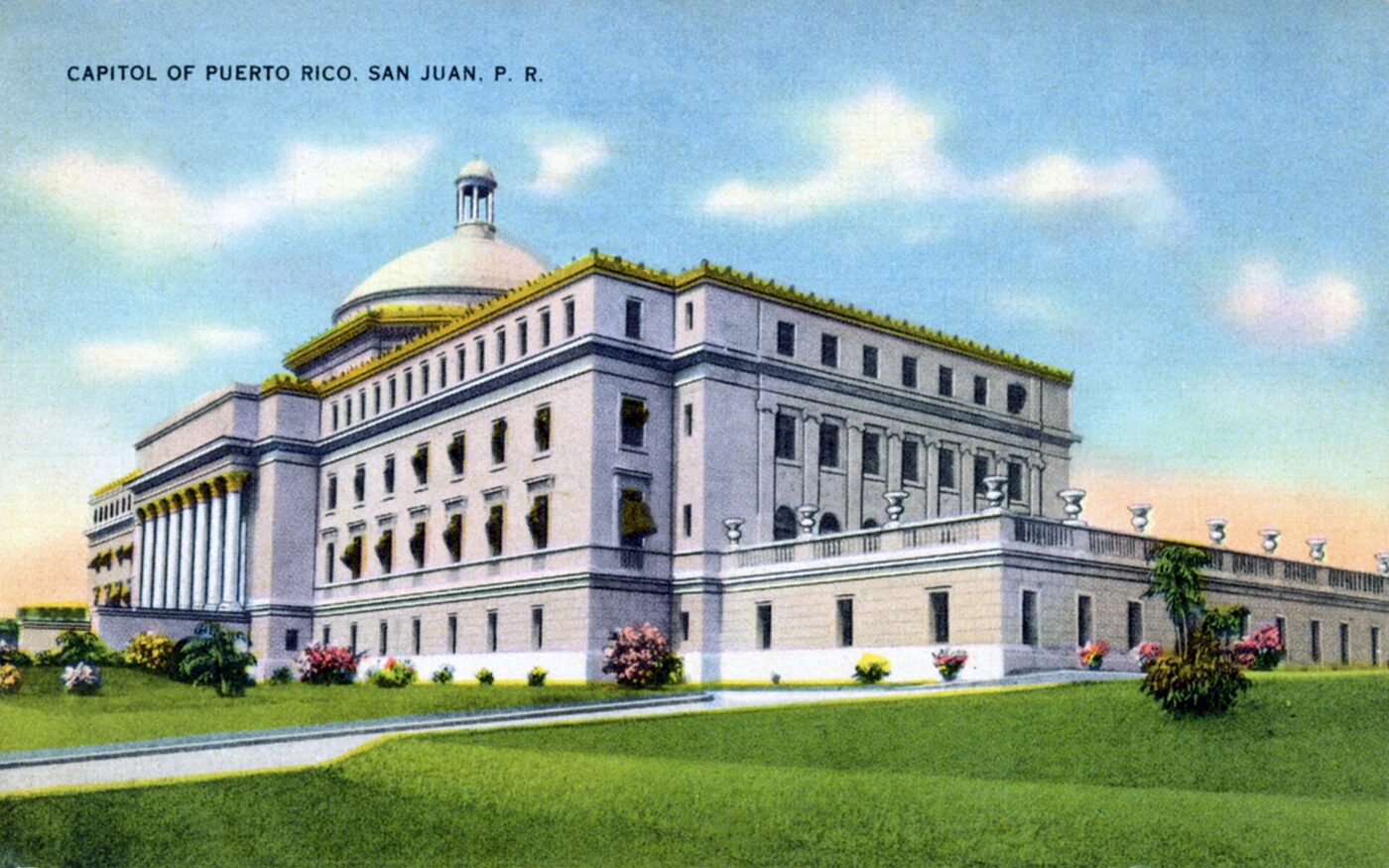 A white neoclassical capitol building with a dome and a columned portico, seen from one corner across lawns on a colour-tinted postcard captioned &lsquo;Capitol of Puerto Rico, San Juan, P. R.&rsquo;