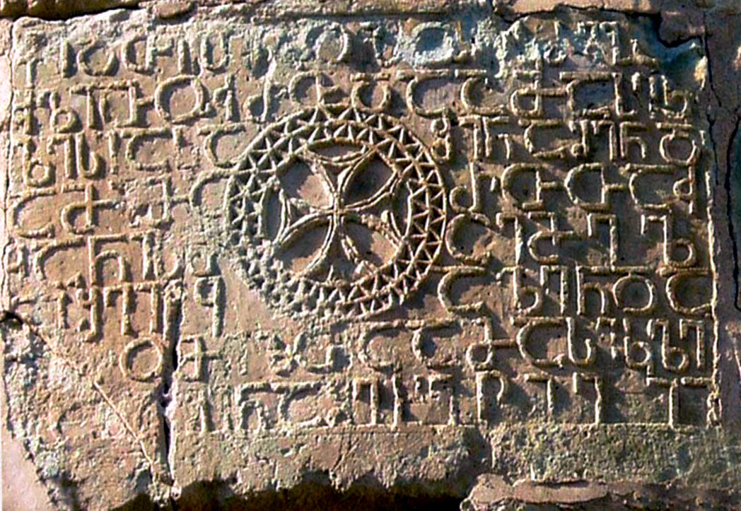 Weathered stone slab carved with rounded, geometric Georgian Asomtavruli letters in horizontal lines, with an ornamented circular cross set into the middle of the text.