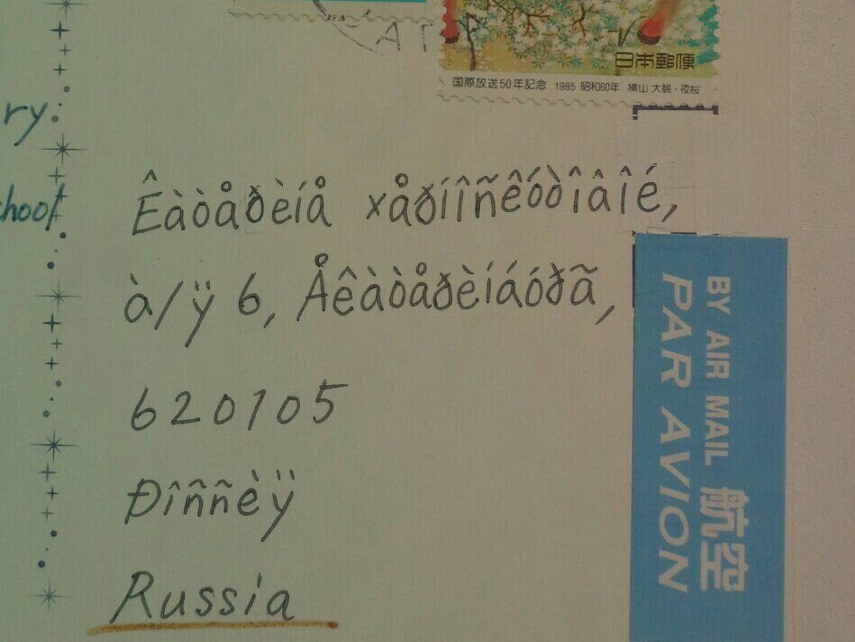 A handwritten postcard address in which the lines above the postcode and the word Russia consist of accented Latin letters rather than words, beside a Japanese stamp and a par avion label.