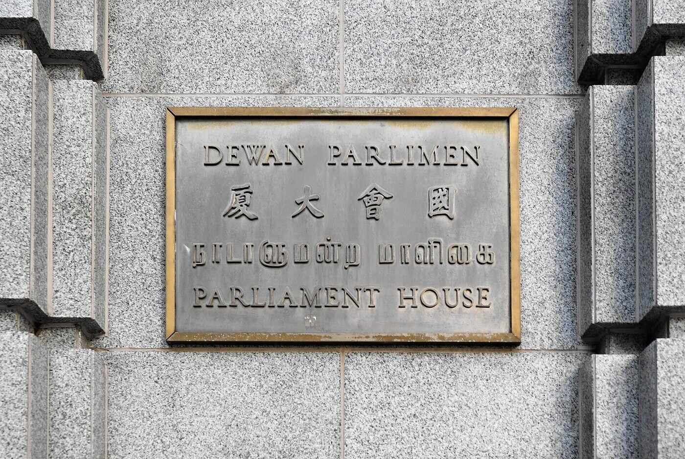 A metal sign reading Parliament House in English, Chinese, Malay and Tamil, mounted on a wall.