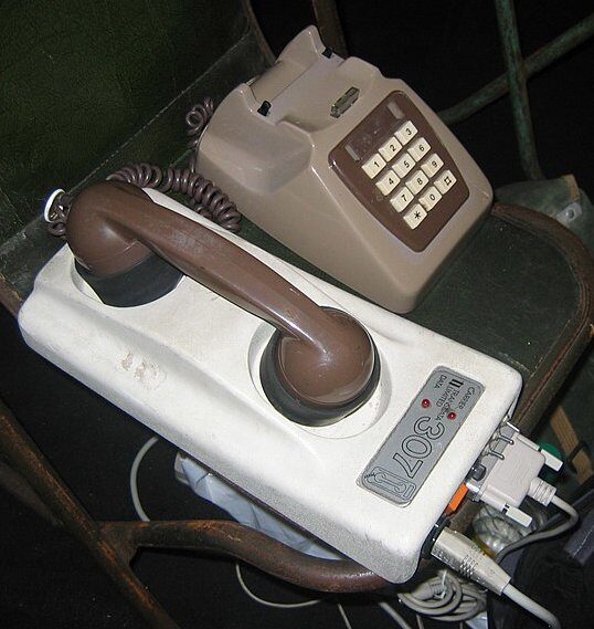 An analogue acoustic coupler modem with a telephone handset pressed into its rubber cups.