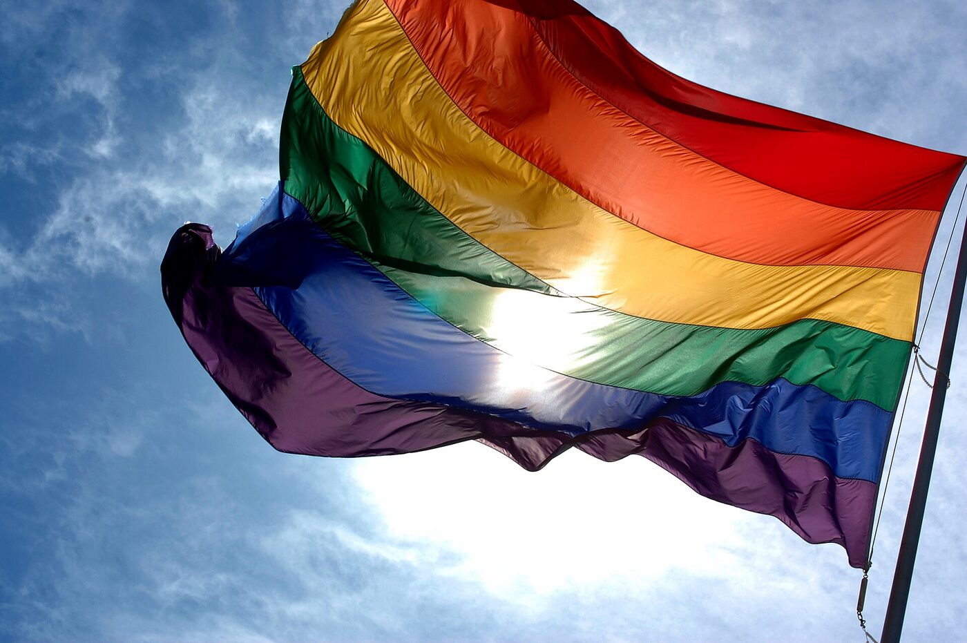 A rainbow pride flag flying against a blue sky.